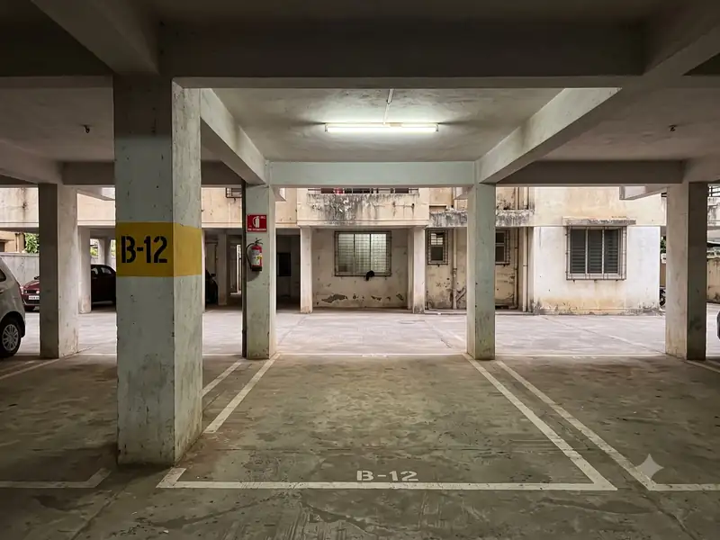 Empty numbered parking slot B-12 in an apartment stilt area, marked with white lines